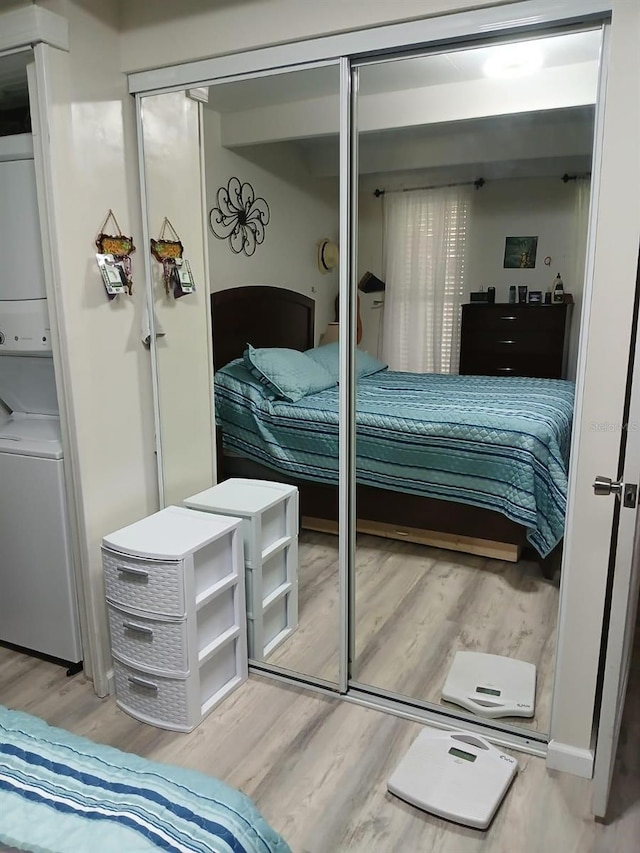 bedroom featuring hardwood / wood-style floors, stacked washer / drying machine, and a closet