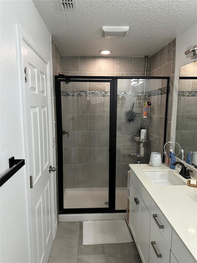 bathroom with a textured ceiling, vanity, tile patterned floors, and walk in shower