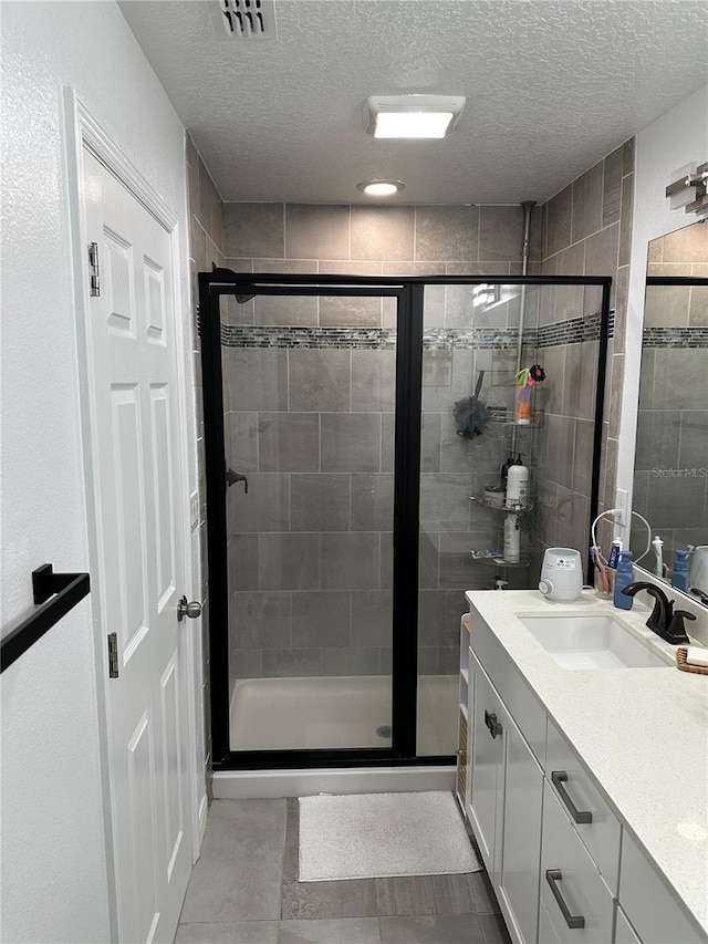 bathroom featuring tile patterned floors, vanity, a shower with shower door, and a textured ceiling