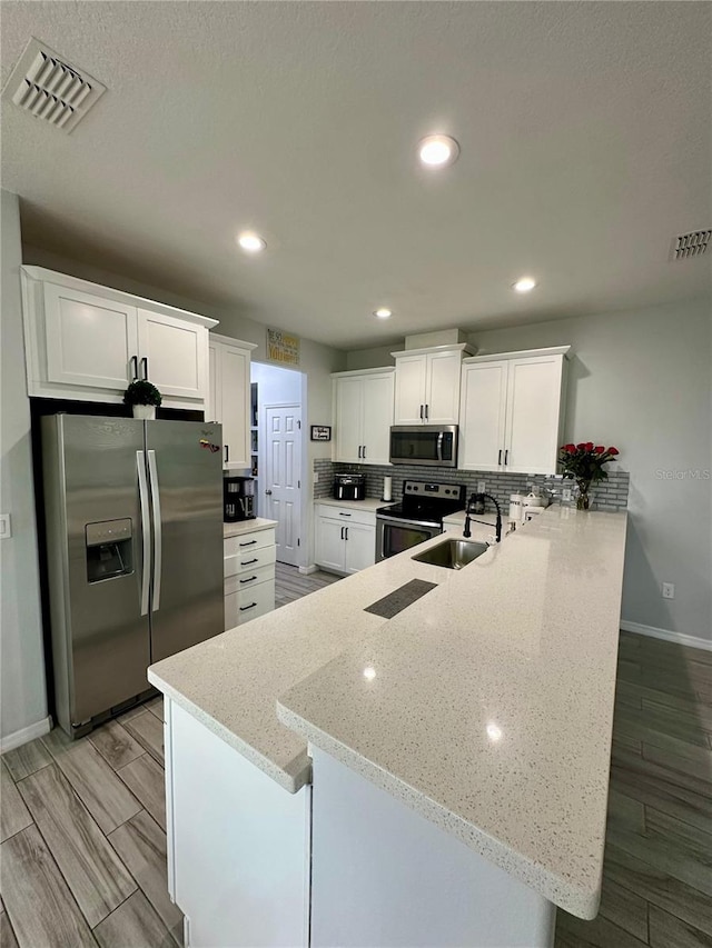 kitchen featuring light stone countertops, sink, kitchen peninsula, white cabinets, and appliances with stainless steel finishes