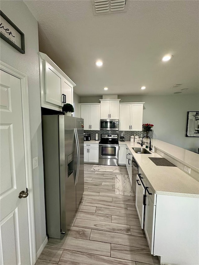 kitchen featuring kitchen peninsula, stainless steel appliances, white cabinetry, and sink