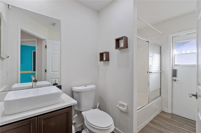 full bathroom featuring bath / shower combo with glass door, vanity, wood-type flooring, and toilet