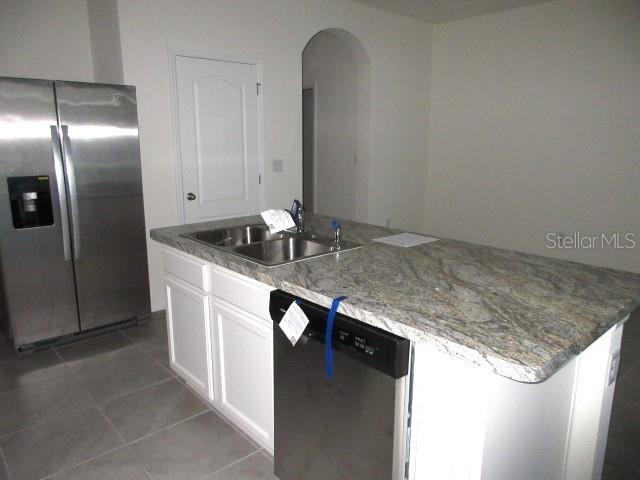 kitchen featuring a kitchen island with sink, white cabinets, sink, dark tile patterned floors, and appliances with stainless steel finishes