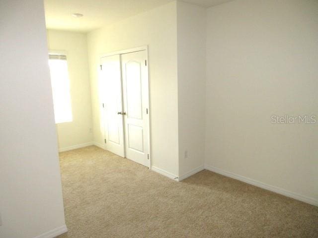 unfurnished bedroom with light colored carpet and a closet