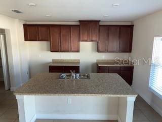 kitchen with a kitchen island with sink, sink, light tile patterned flooring, and light stone counters