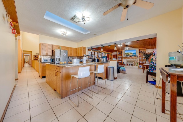 kitchen with stainless steel fridge, a center island, ceiling fan, and light tile patterned floors