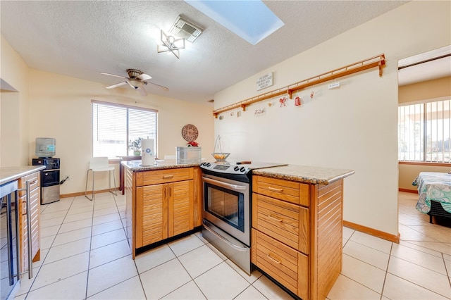 kitchen with a textured ceiling, stainless steel electric range oven, ceiling fan, and light tile patterned flooring