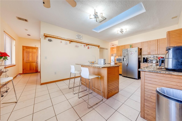 kitchen featuring light stone countertops, light tile patterned floors, a kitchen island, a kitchen bar, and stainless steel fridge with ice dispenser