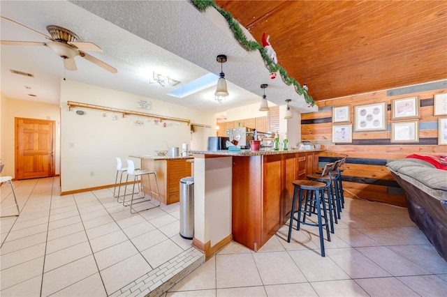 kitchen with ceiling fan, pendant lighting, light tile patterned floors, a breakfast bar area, and wood walls