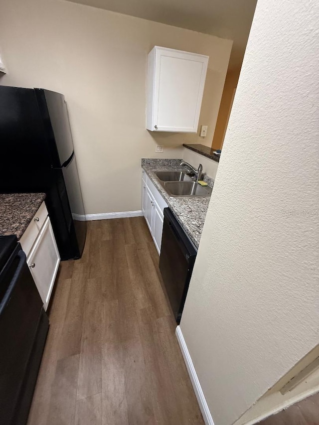 kitchen featuring dark hardwood / wood-style flooring, dark stone counters, sink, black appliances, and white cabinets