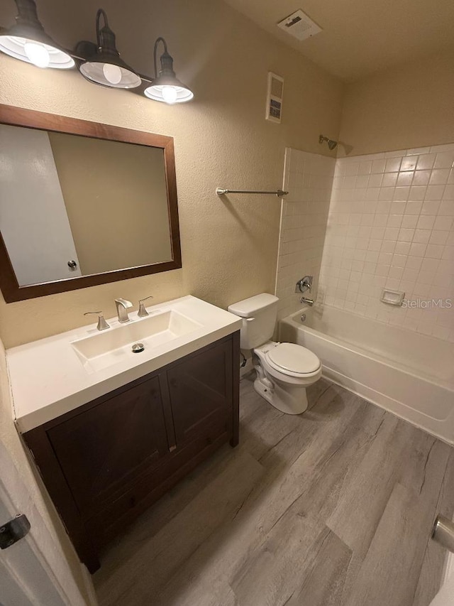 full bathroom with vanity, wood-type flooring, tiled shower / bath combo, and toilet