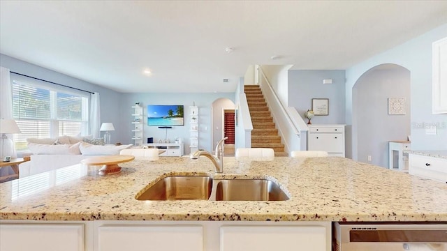 kitchen with dishwashing machine, white cabinetry, light stone countertops, and sink