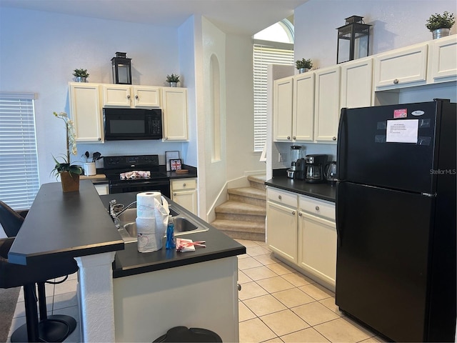 kitchen with sink, a kitchen island, light tile patterned flooring, white cabinets, and black appliances