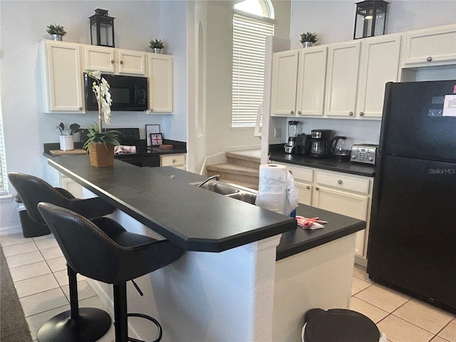 kitchen featuring a kitchen breakfast bar, sink, black appliances, white cabinets, and light tile patterned flooring