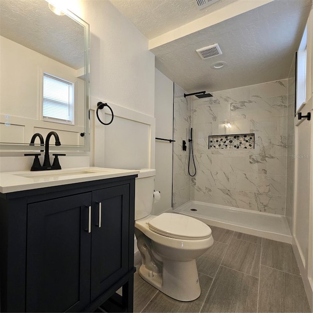 bathroom featuring vanity, toilet, a textured ceiling, and a tile shower