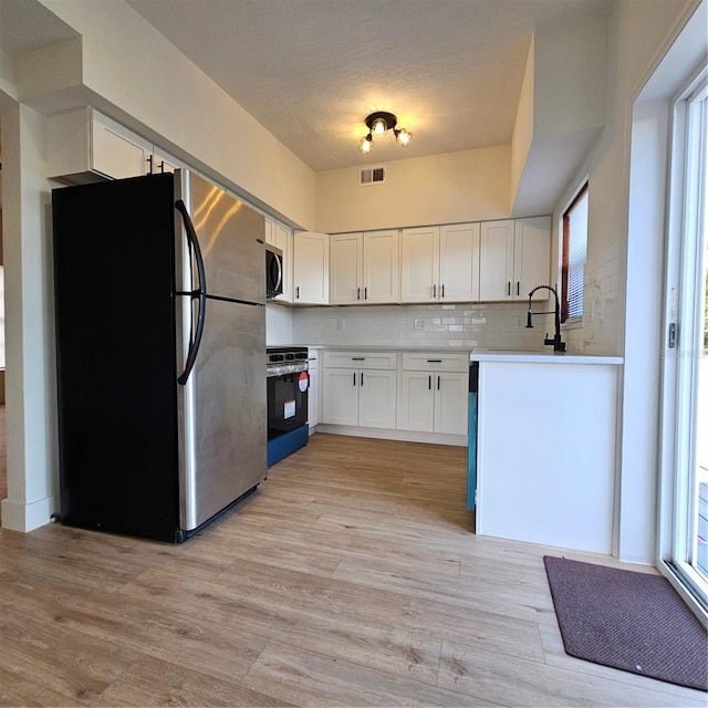 kitchen featuring white cabinets, appliances with stainless steel finishes, backsplash, and plenty of natural light