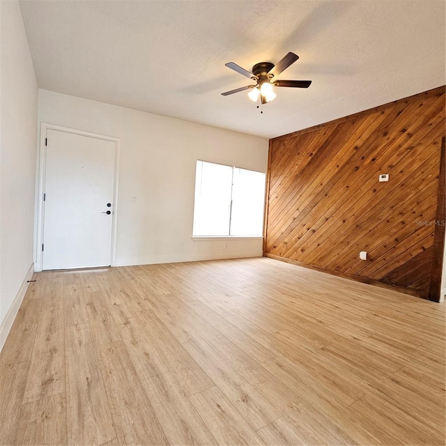 empty room with a textured ceiling, light wood-type flooring, ceiling fan, and wood walls