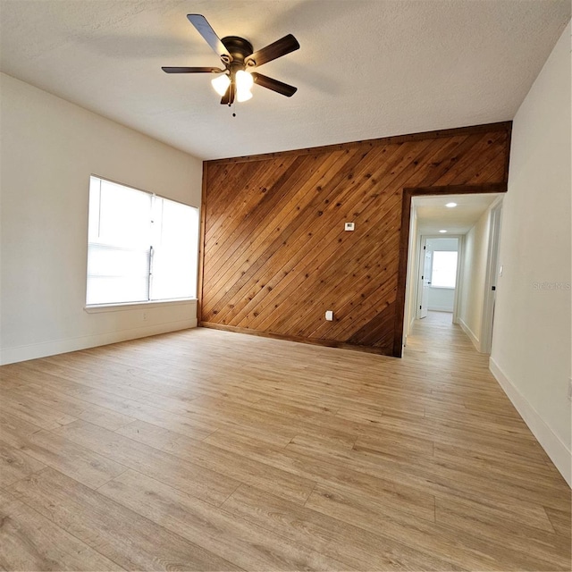 unfurnished room featuring ceiling fan, light hardwood / wood-style floors, a textured ceiling, and wooden walls