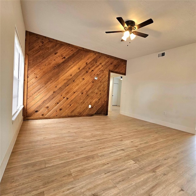 unfurnished room featuring light hardwood / wood-style floors, ceiling fan, and wooden walls