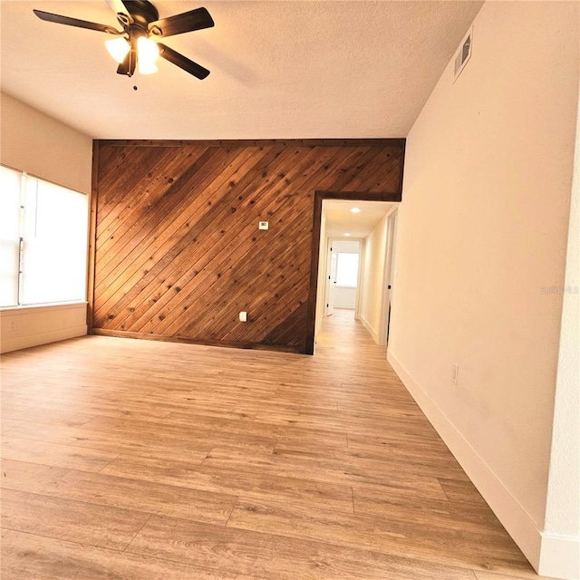 spare room with ceiling fan, wood walls, light wood-type flooring, and a textured ceiling