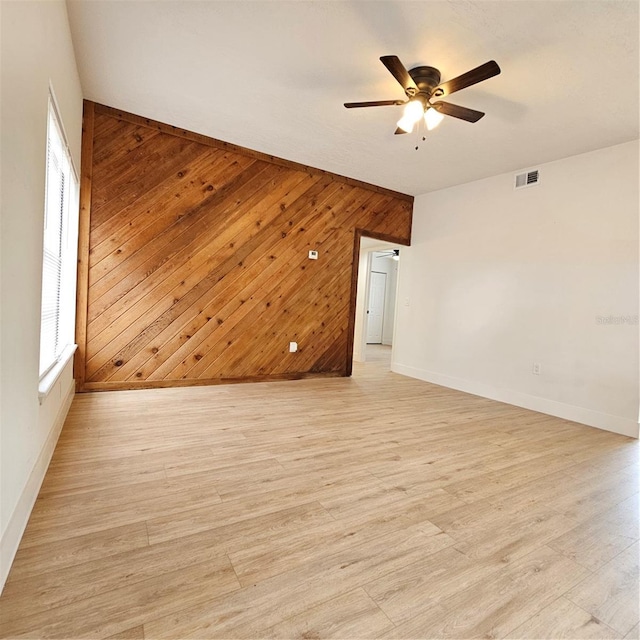 empty room with a wealth of natural light, wooden walls, ceiling fan, and light hardwood / wood-style floors