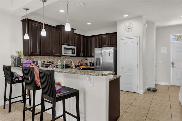 kitchen featuring kitchen peninsula, appliances with stainless steel finishes, light stone countertops, hanging light fixtures, and a breakfast bar area