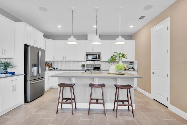 kitchen with decorative backsplash, stainless steel appliances, decorative light fixtures, white cabinetry, and an island with sink