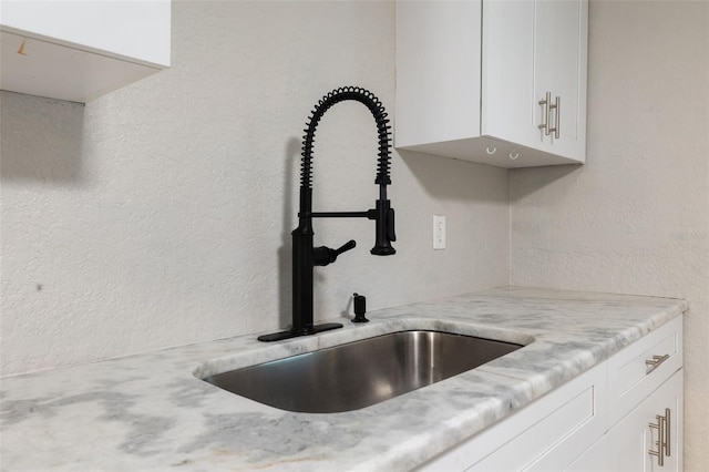 room details featuring white cabinets, light stone counters, and sink