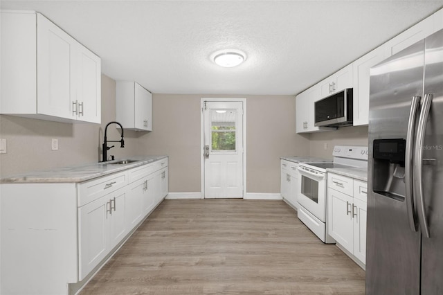 kitchen with white cabinets, appliances with stainless steel finishes, light stone counters, and sink