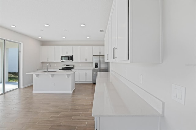 kitchen with white cabinetry, sink, stainless steel appliances, an island with sink, and a breakfast bar