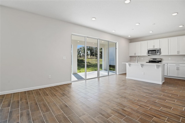 kitchen featuring sink, a kitchen breakfast bar, a center island with sink, white cabinets, and appliances with stainless steel finishes