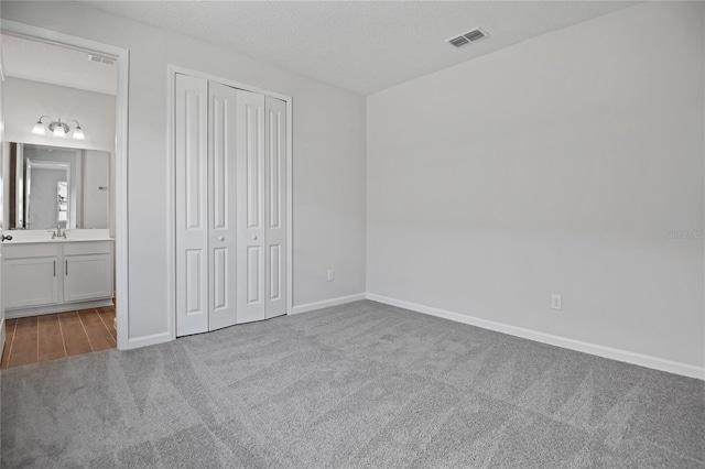 unfurnished bedroom featuring sink, ensuite bathroom, light colored carpet, a textured ceiling, and a closet