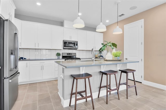 kitchen featuring white cabinetry, sink, hanging light fixtures, stainless steel appliances, and a center island with sink