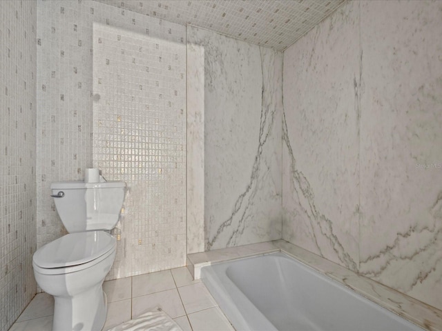 bathroom with tile patterned floors, a bathing tub, toilet, and tile walls