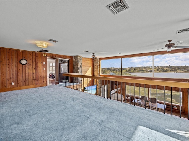 interior space featuring ceiling fan, a water view, carpet floors, and wooden walls