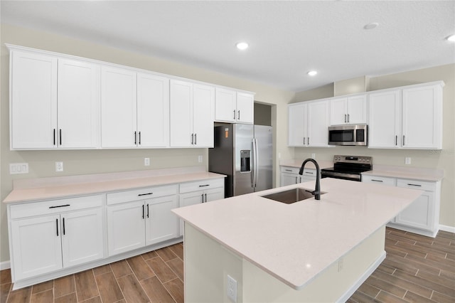 kitchen with white cabinets, appliances with stainless steel finishes, a kitchen island with sink, and sink