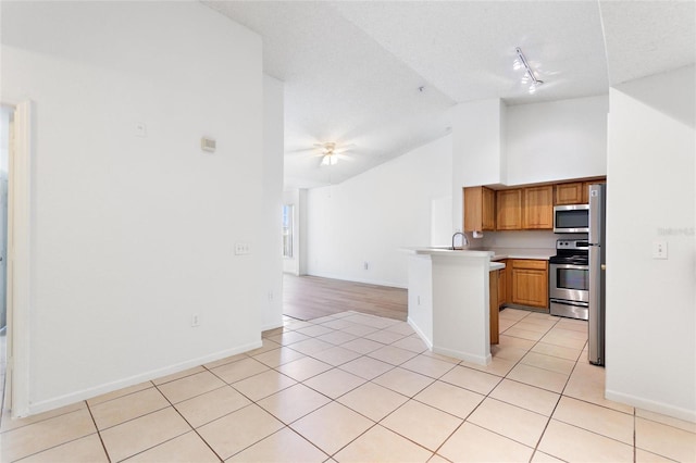 kitchen with lofted ceiling, ceiling fan, light tile patterned floors, kitchen peninsula, and stainless steel appliances