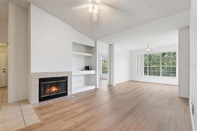 unfurnished living room with a tile fireplace, light wood-type flooring, a textured ceiling, and built in features