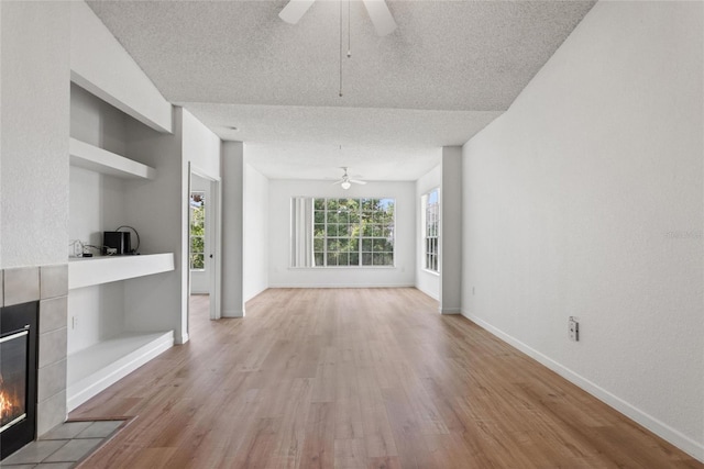 unfurnished living room featuring a textured ceiling, light hardwood / wood-style flooring, ceiling fan, and a tiled fireplace