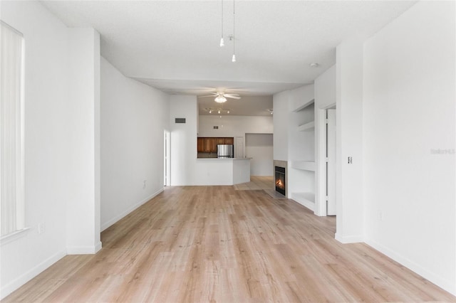 unfurnished living room with light hardwood / wood-style floors, built in shelves, ceiling fan, and a towering ceiling