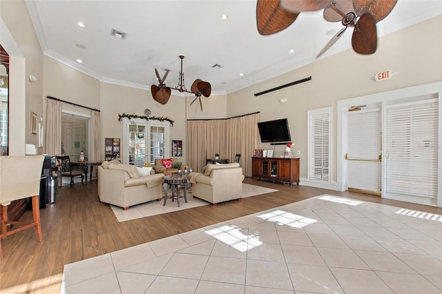 unfurnished living room featuring a towering ceiling, light hardwood / wood-style flooring, ceiling fan, and crown molding