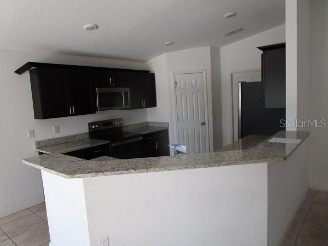 kitchen with kitchen peninsula, light tile patterned floors, light stone countertops, and black appliances