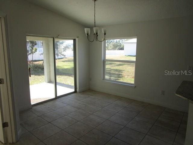 unfurnished dining area featuring lofted ceiling, dark tile patterned floors, and a notable chandelier