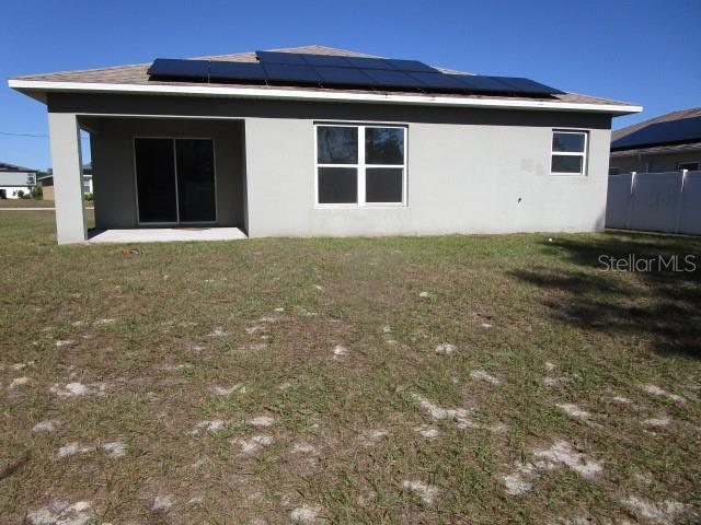 rear view of property featuring solar panels and a yard