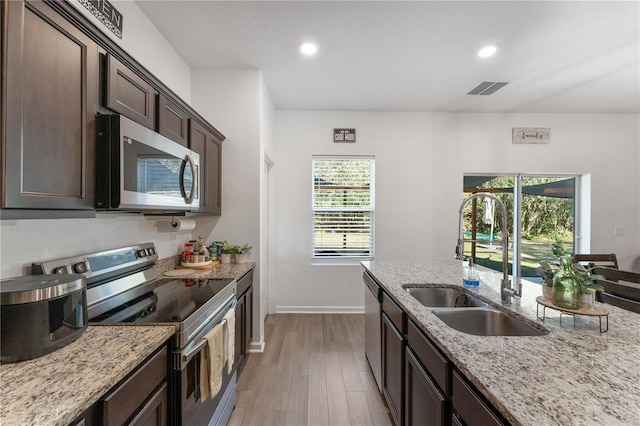 kitchen with light stone countertops, appliances with stainless steel finishes, dark brown cabinets, and sink