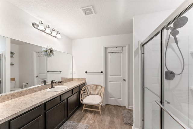 bathroom with an enclosed shower, vanity, a textured ceiling, hardwood / wood-style flooring, and toilet