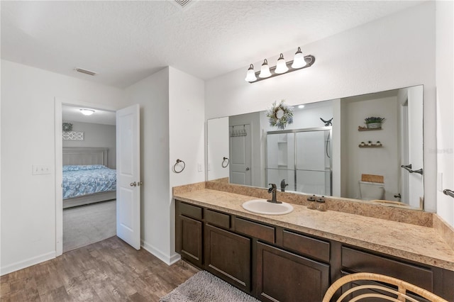 bathroom featuring an enclosed shower, vanity, a textured ceiling, hardwood / wood-style flooring, and toilet