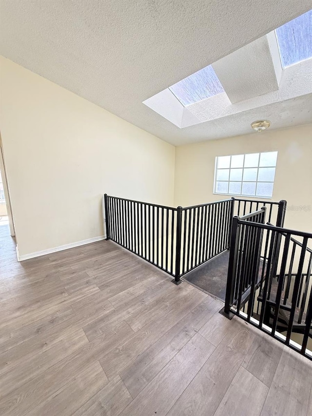 corridor featuring light hardwood / wood-style flooring, a textured ceiling, and a skylight