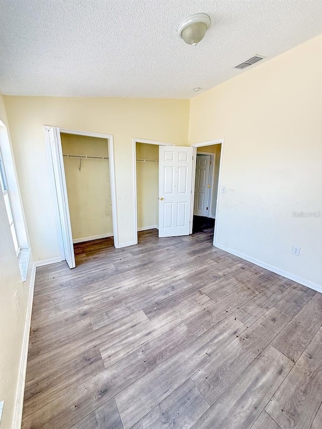 unfurnished bedroom featuring lofted ceiling, a textured ceiling, light hardwood / wood-style flooring, and two closets