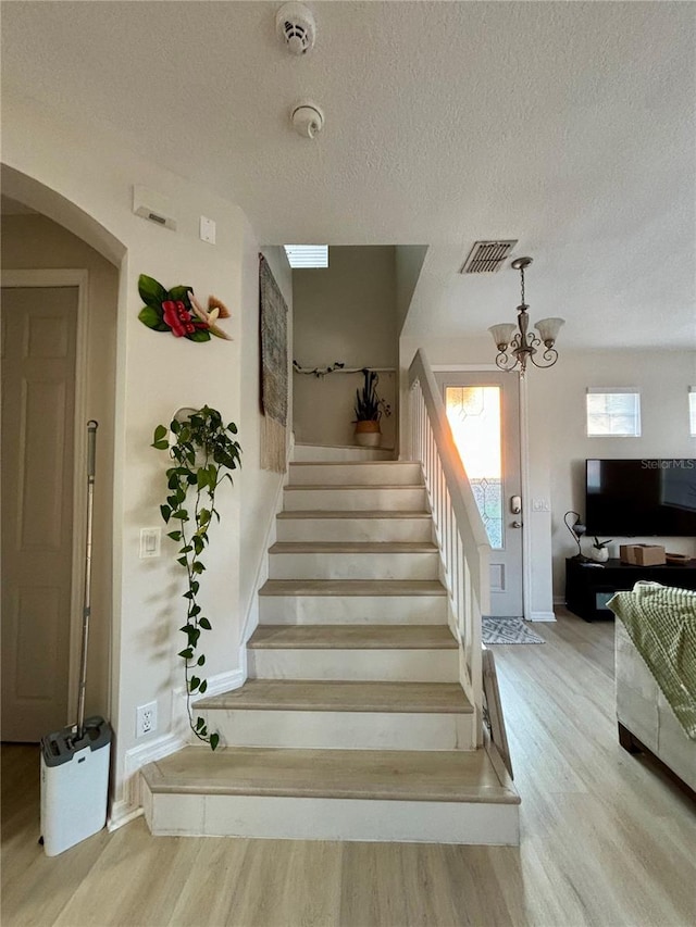 stairway featuring a textured ceiling, hardwood / wood-style flooring, and a notable chandelier